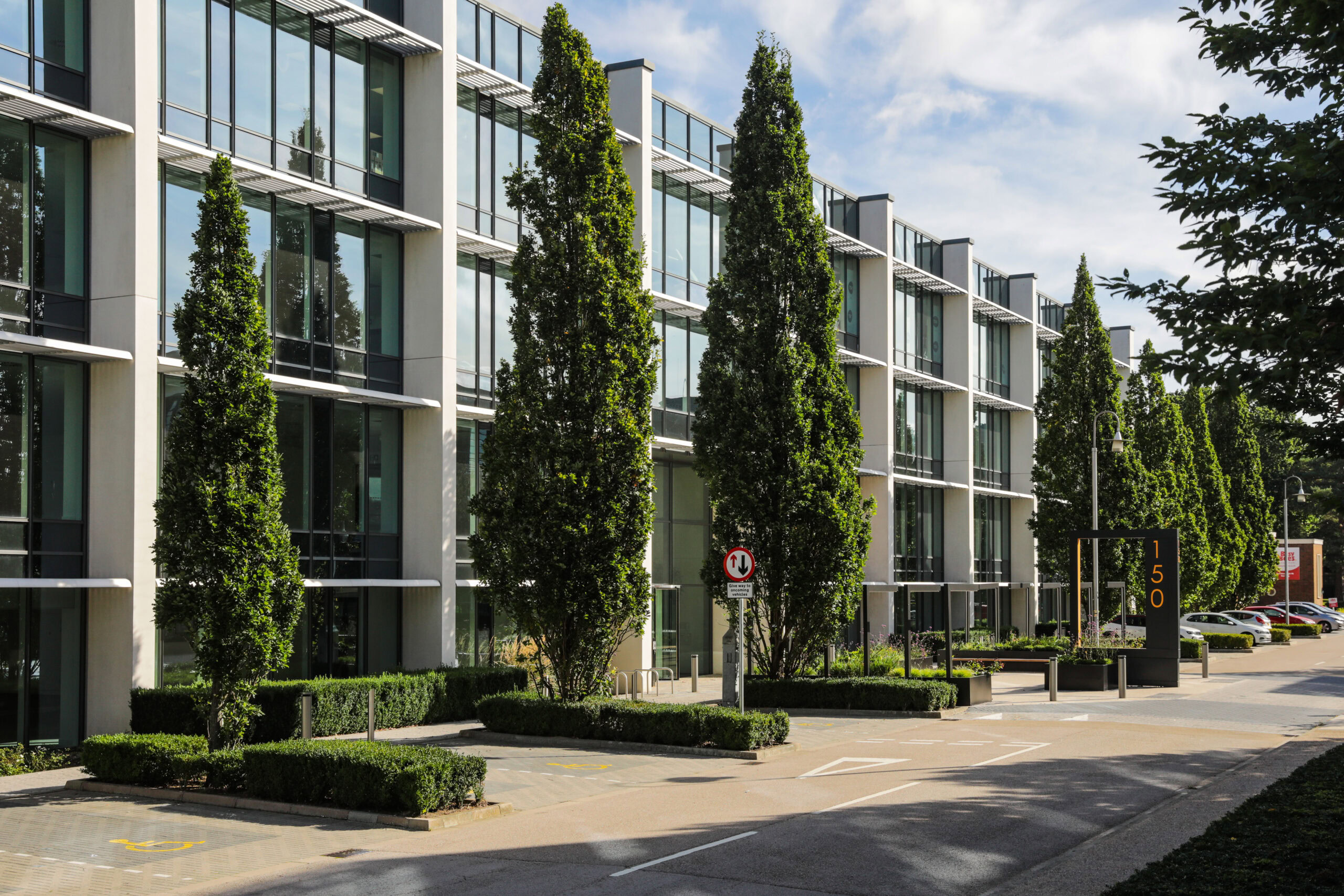 A modern office building features large windows and is surrounded by tall trees