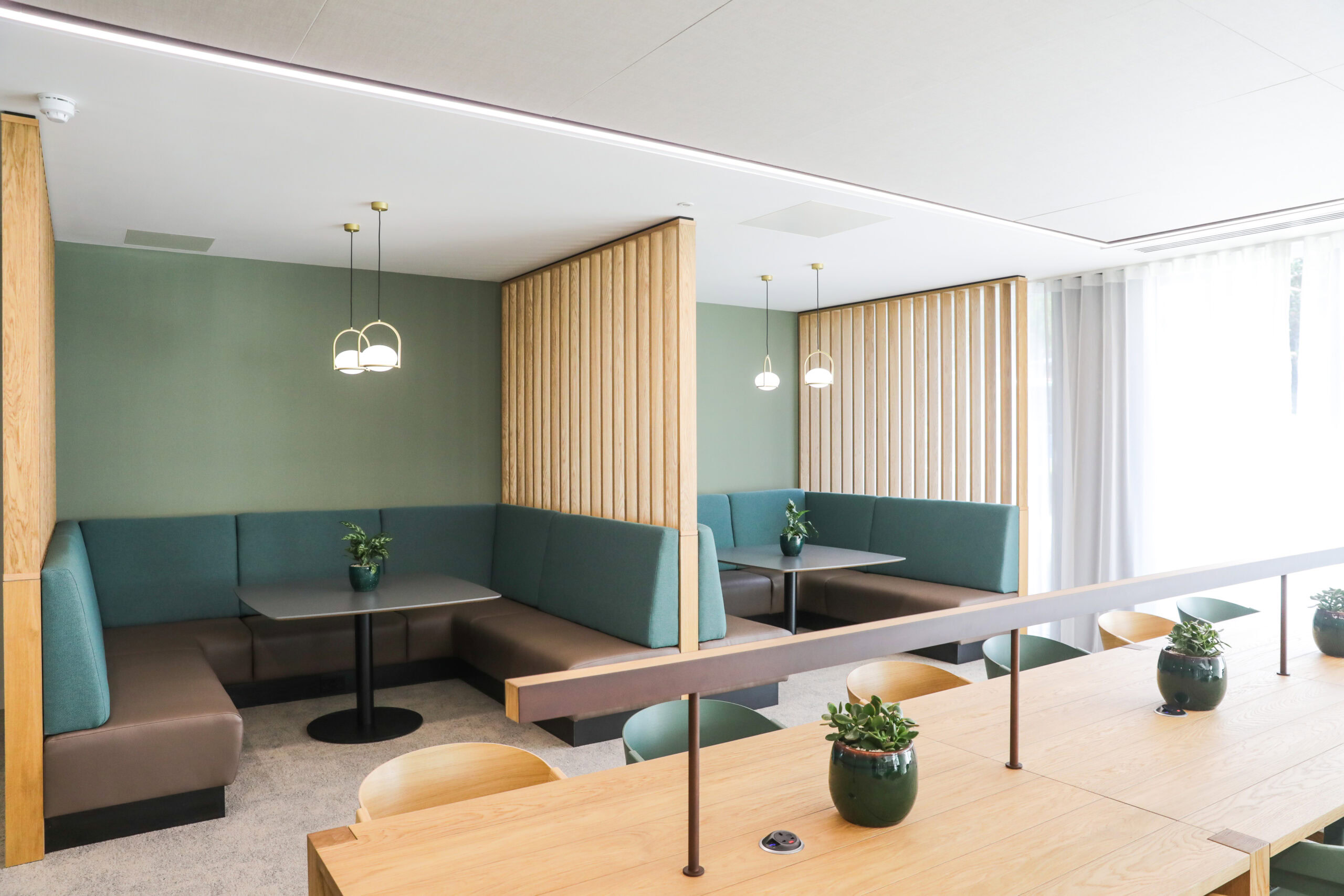 A modern office space features a seating area with wooden tables, green booths, and plants
