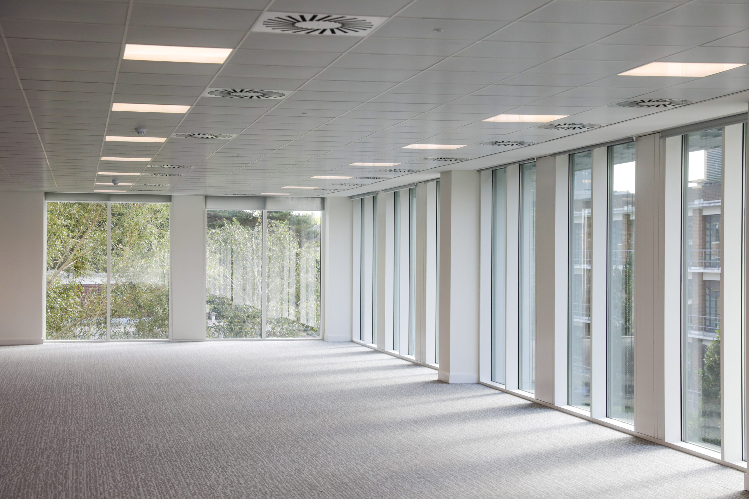 Office space in an office building with large windows, a carpeted floor, and ceiling lights
