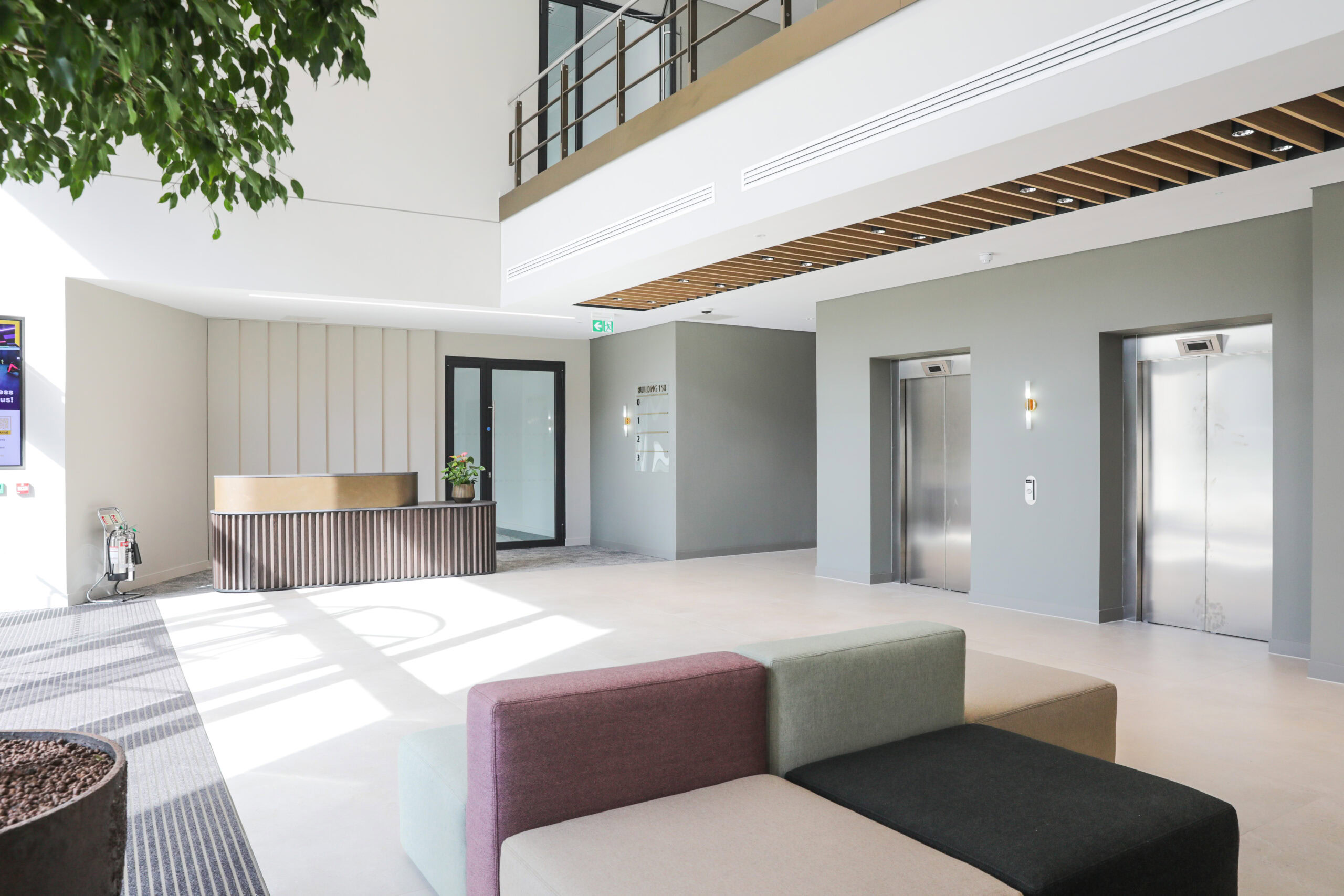 Modern office lobby in a business park featuring a reception desk, two elevators, and a seating area