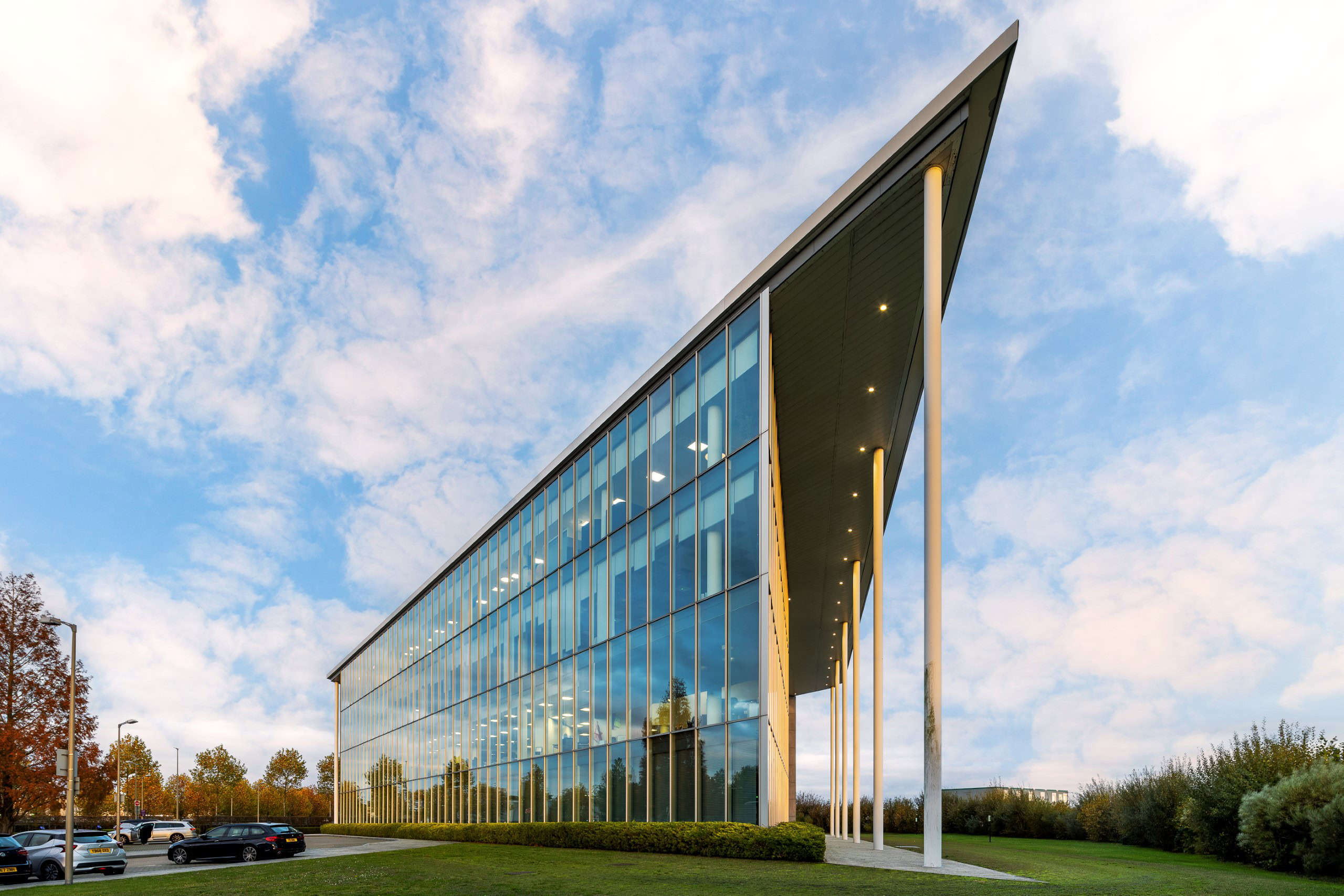A modern glass office building with a triangular roof stands prominently in a business park