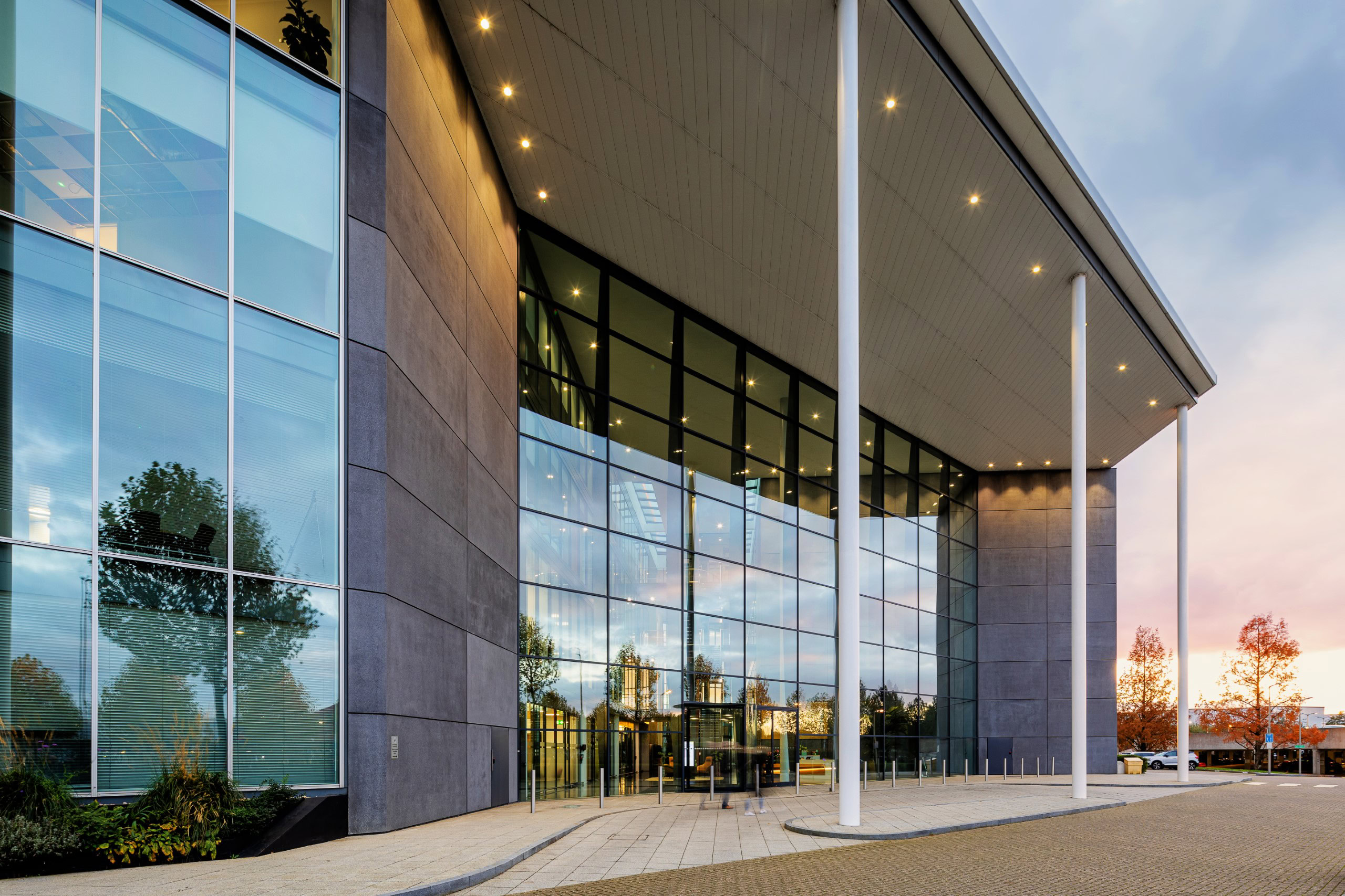 Modern office building facade with large glass windows, white columns, and a paved entrance