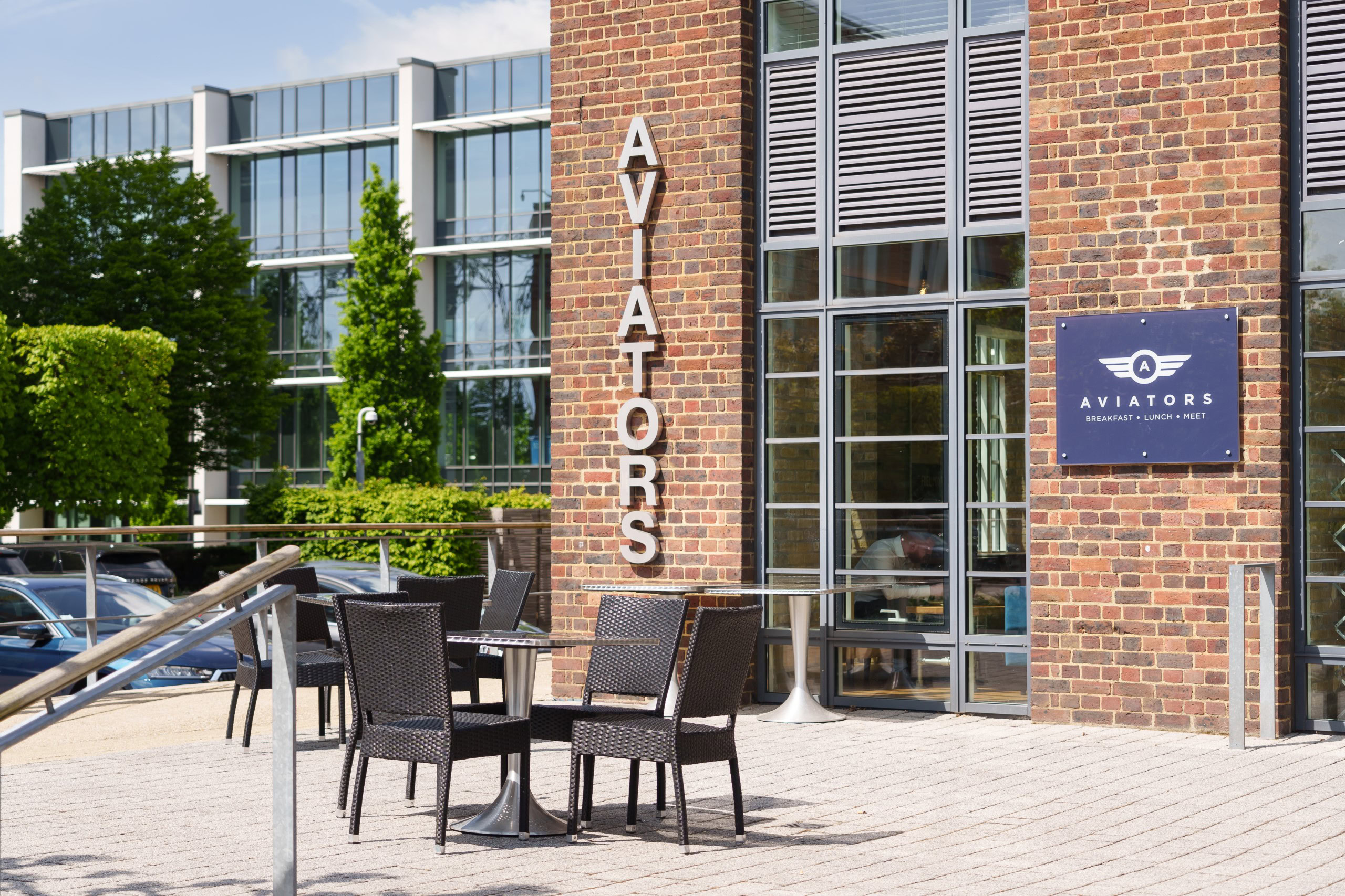 The outdoor seating area of Aviators cafe features chairs and tables next to an office building