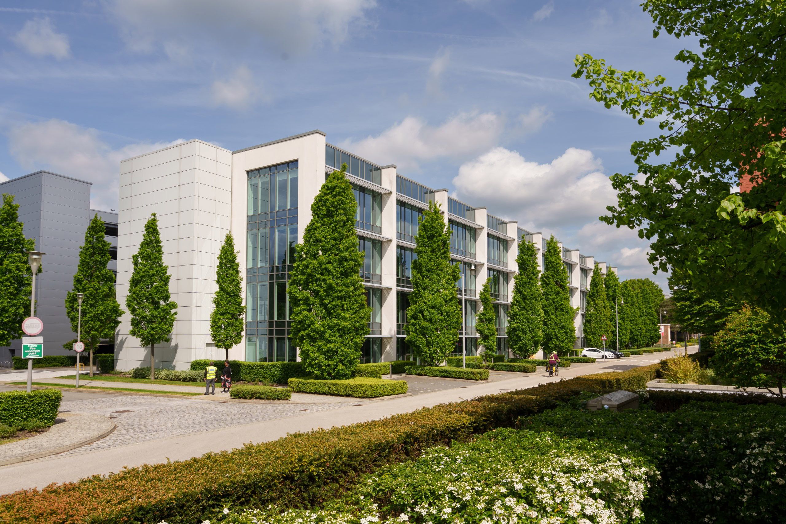 An office building with tall windows is nestled in a business park surrounded by green trees