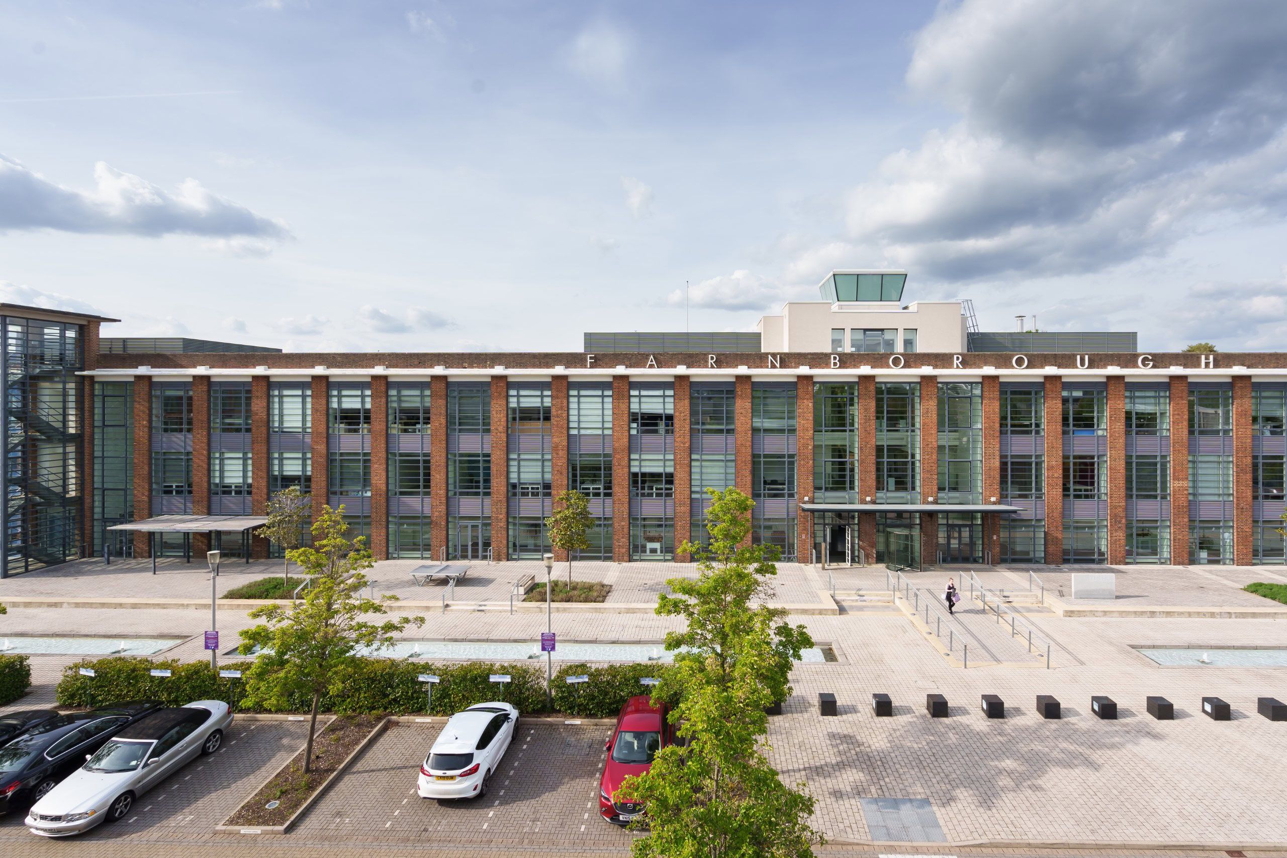Modern office building with a glass and brick facade, surrounded by parked cars and trees
