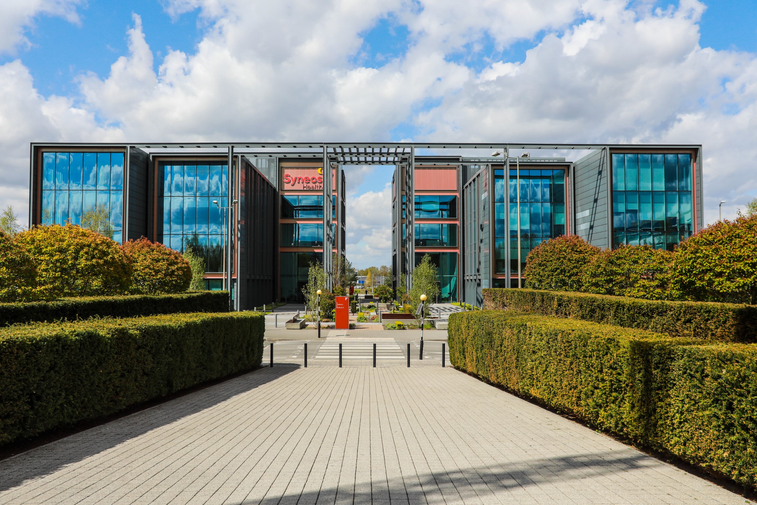 Modern office building with large glass windows, surrounded by trimmed hedges and a paved walkway