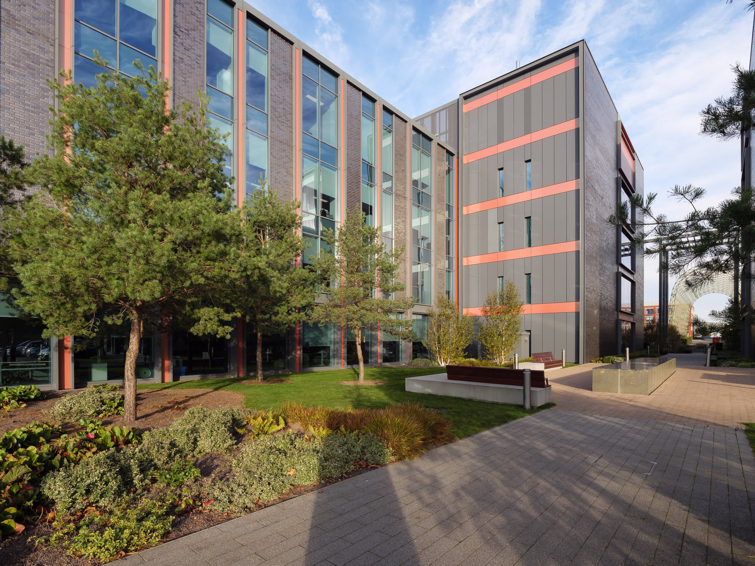 A modern office building stands within a business park, surrounded by landscaped greenery