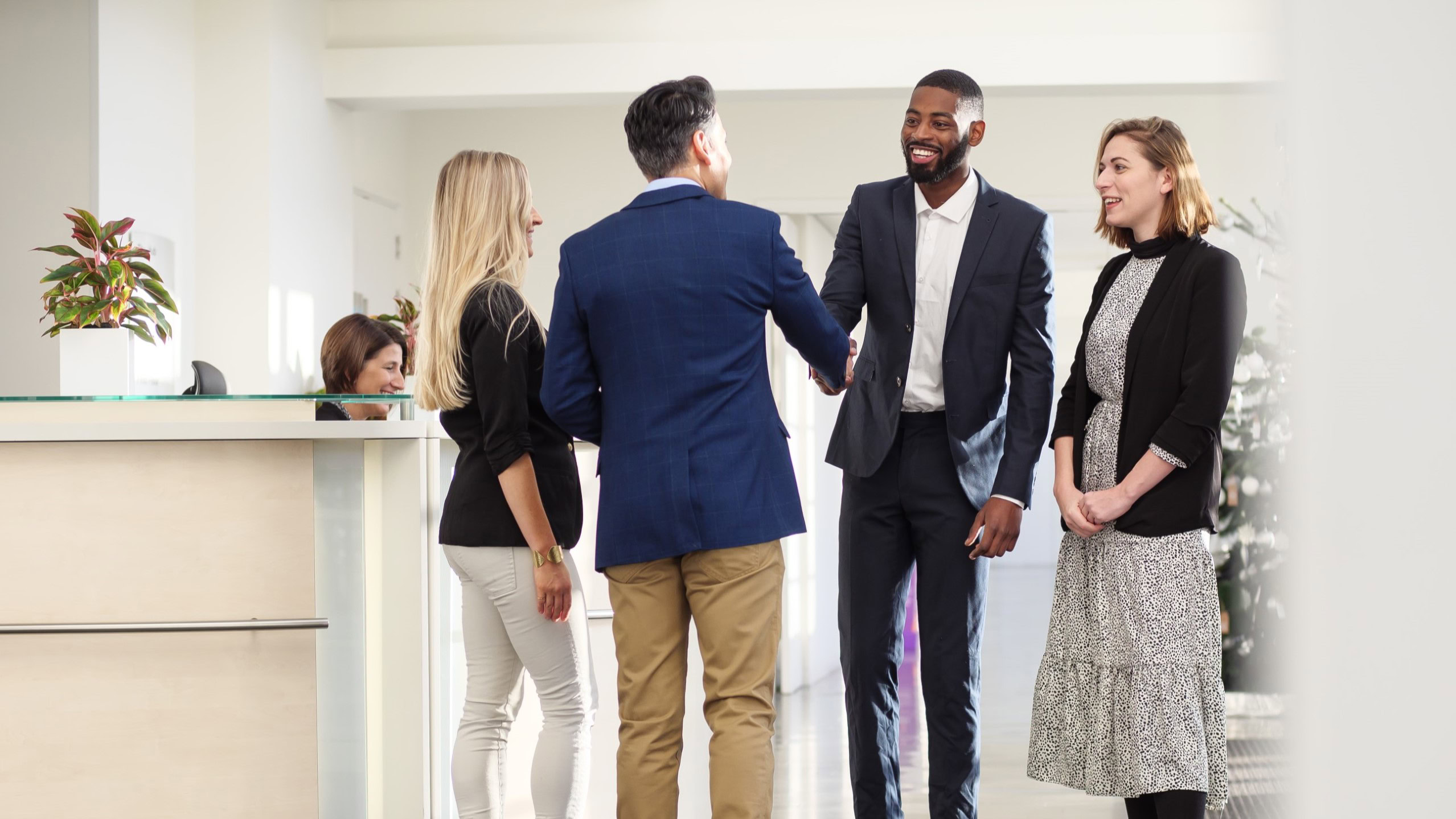 Four people are standing in an office building, greeting each other