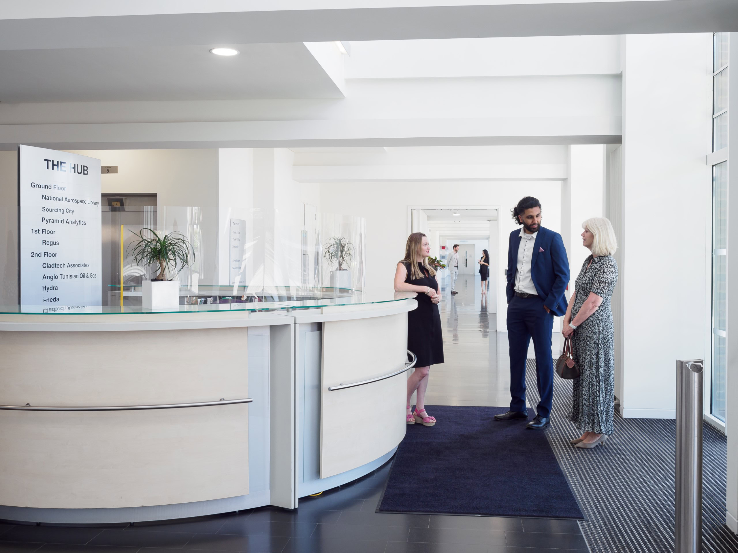 Three people stand and converse near a circular reception desk in a modern office space