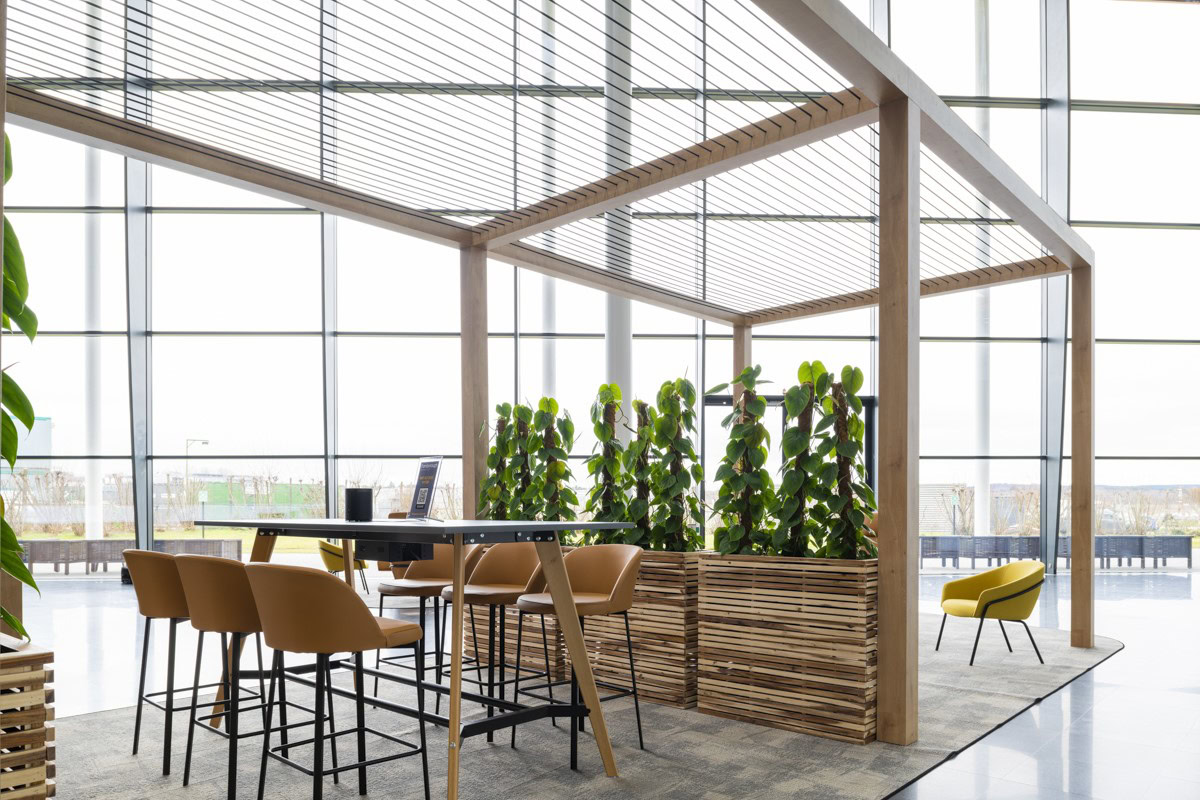 A modern office space features tall tables, barstools, a yellow chair, and lush green plants
