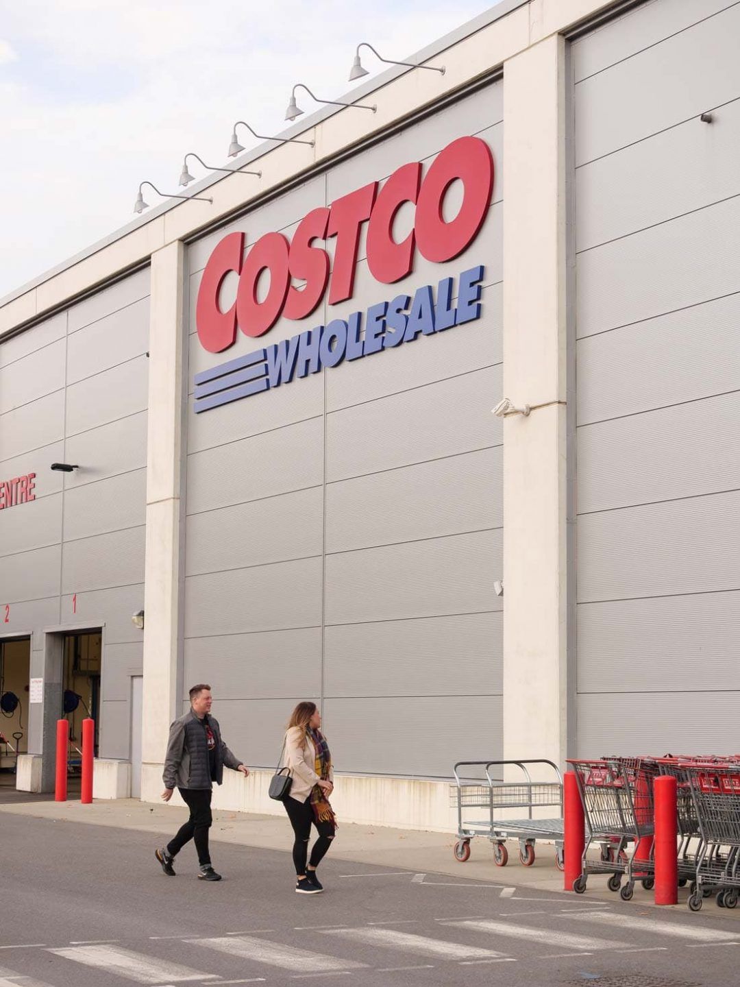 A man and woman stroll past a sprawling Costco Wholesale building
