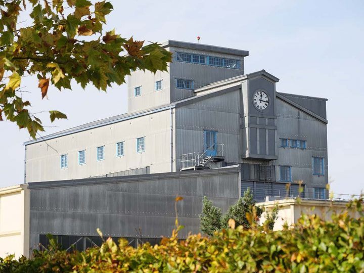 A large industrial office building with a clock on the facade is nestled within a lush business park
