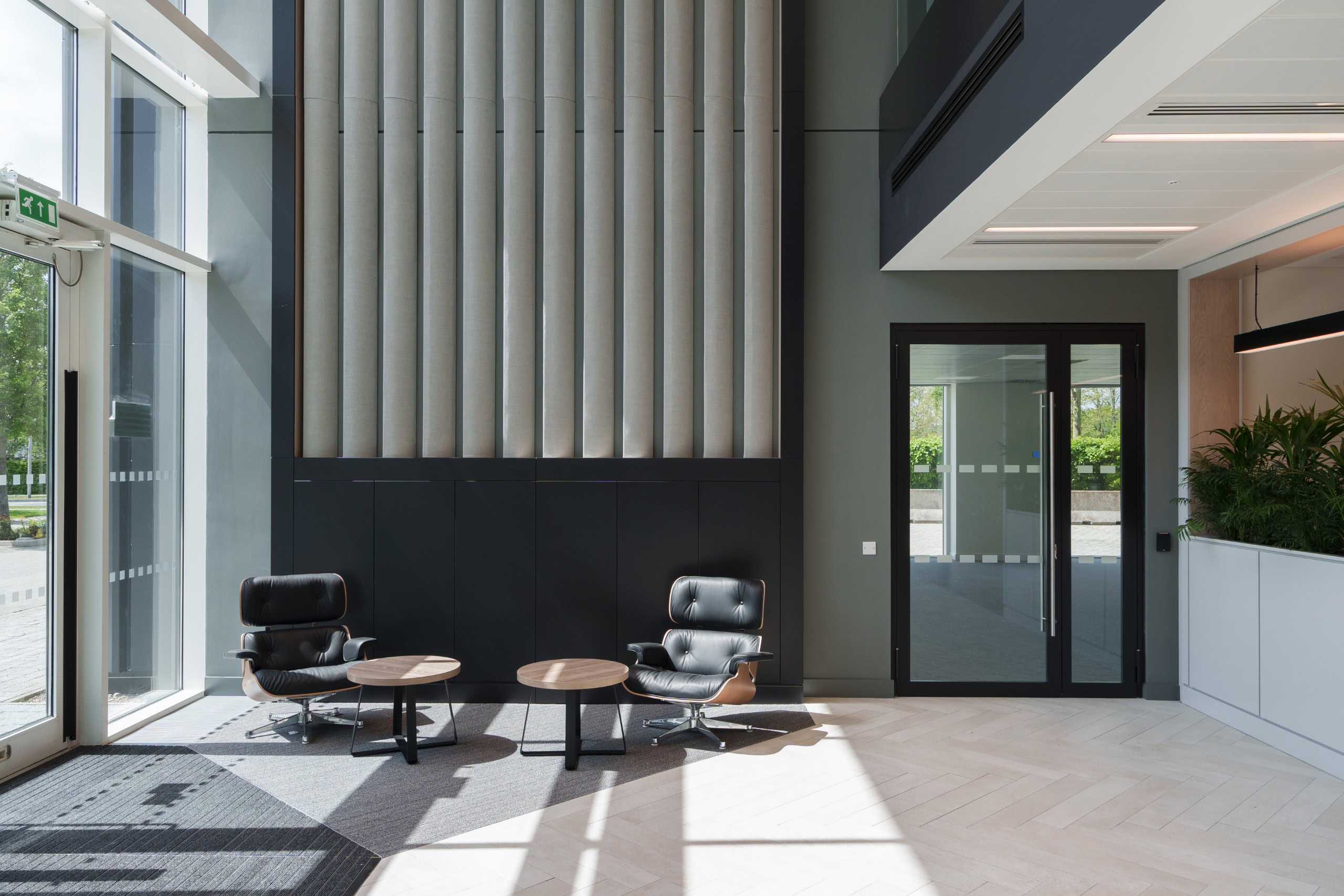 A modern office lobby with black chairs and tables are next to large windows streaming natural light