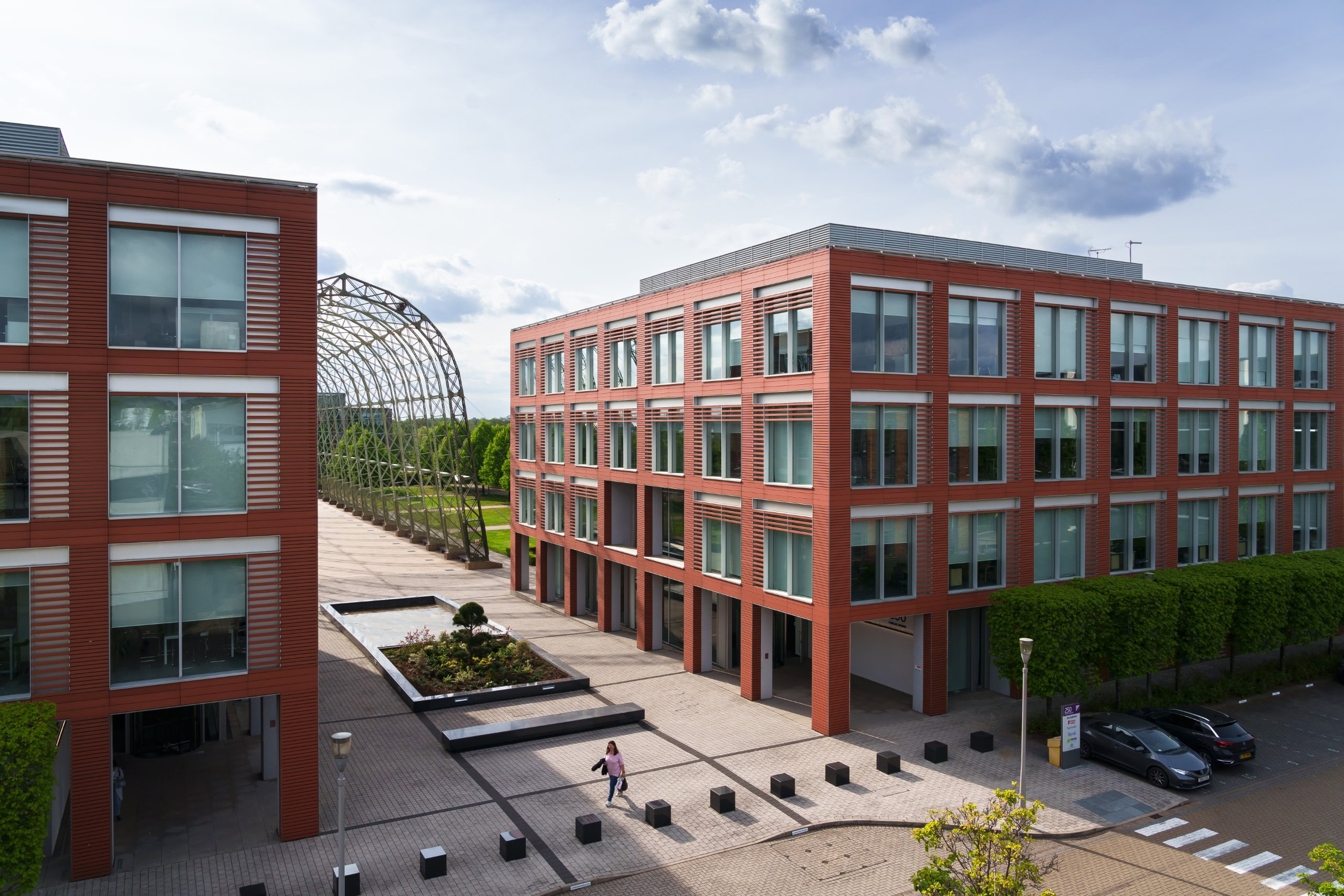 A business park featuring two red brick office buildings with large windows, separated by a walkway