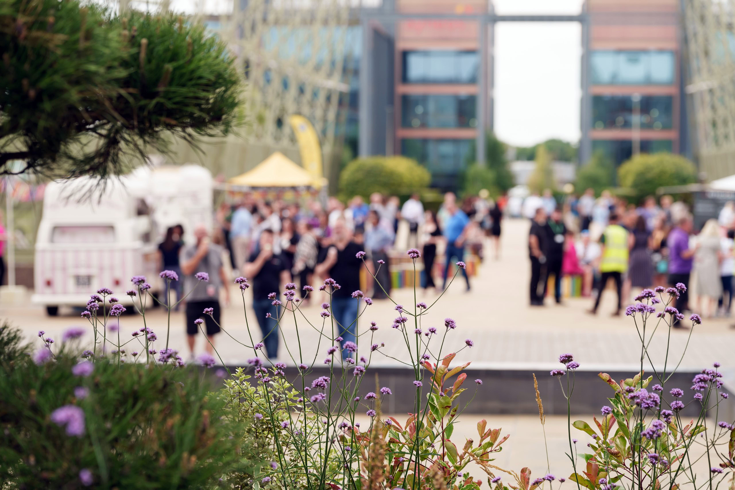People walking and gathering on a plaza, with an office building in the background.
