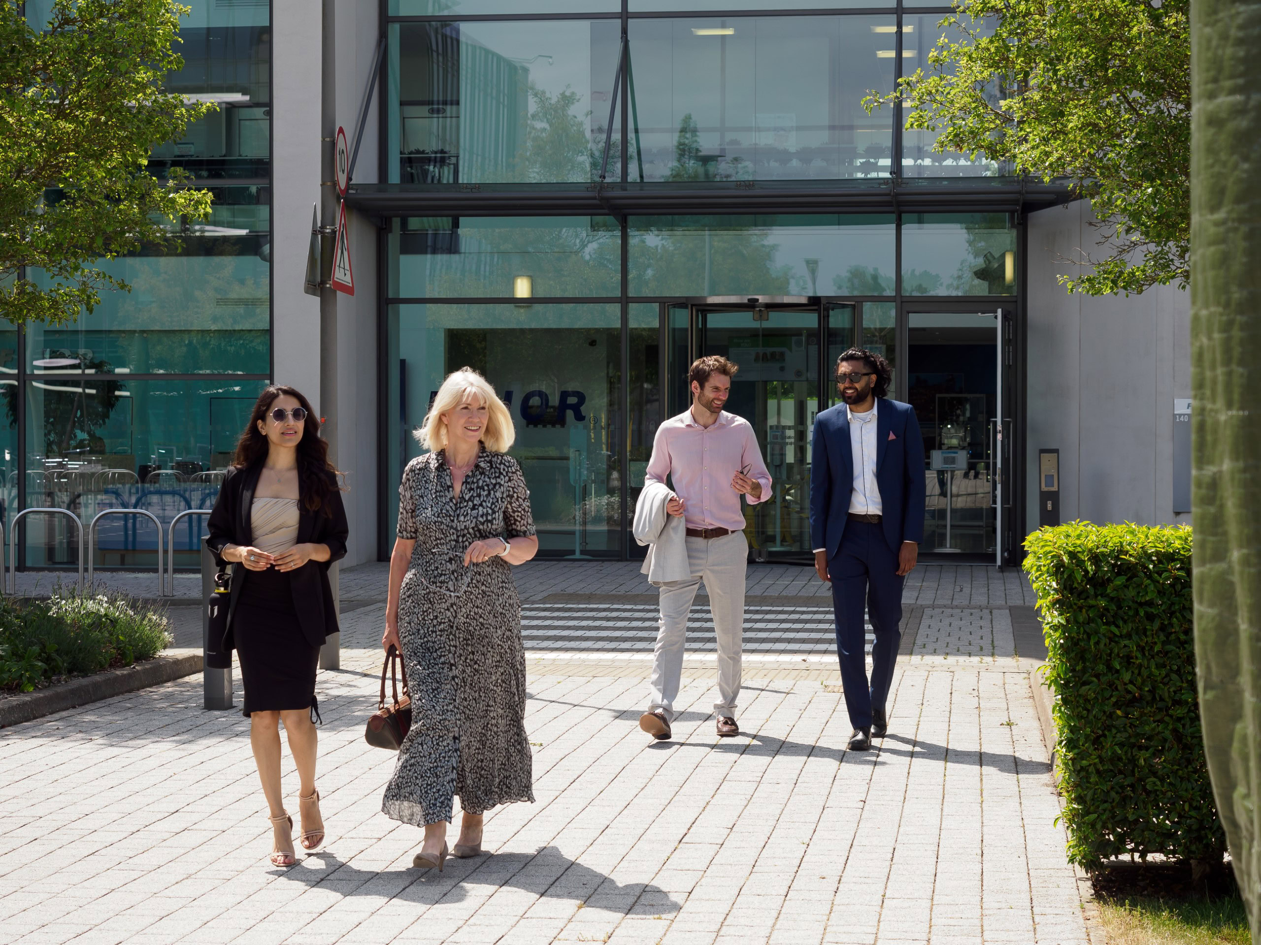Four people walking outside a modern office space, with glass windows and greenery around