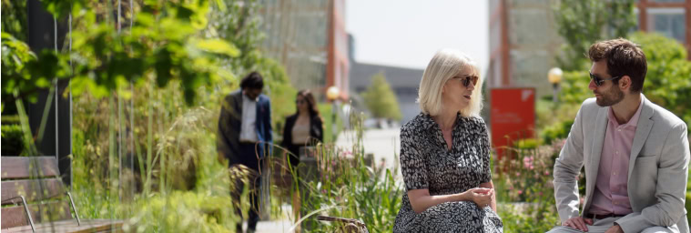 Two people sit and talk on a bench in an outdoor garden area