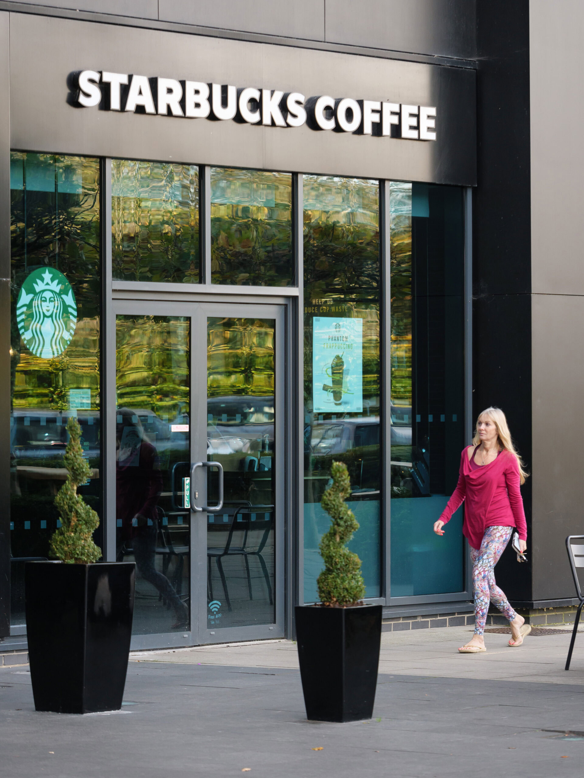 A person in a pink hoodie walks past a Starbucks Coffee storefront between sleek office buildings