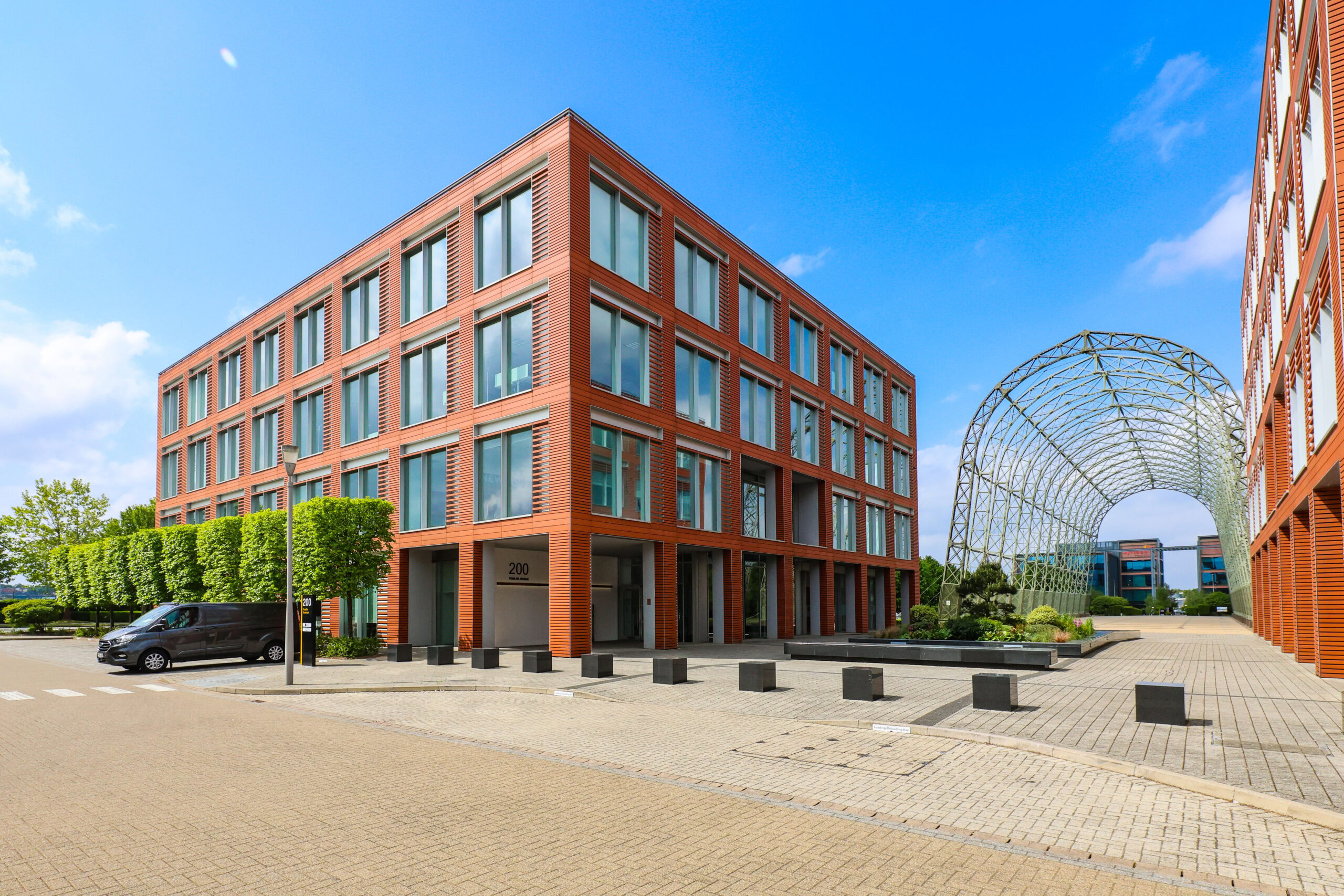 Modern office building with large windows and red panels next to a metal arch structure on a clear day.