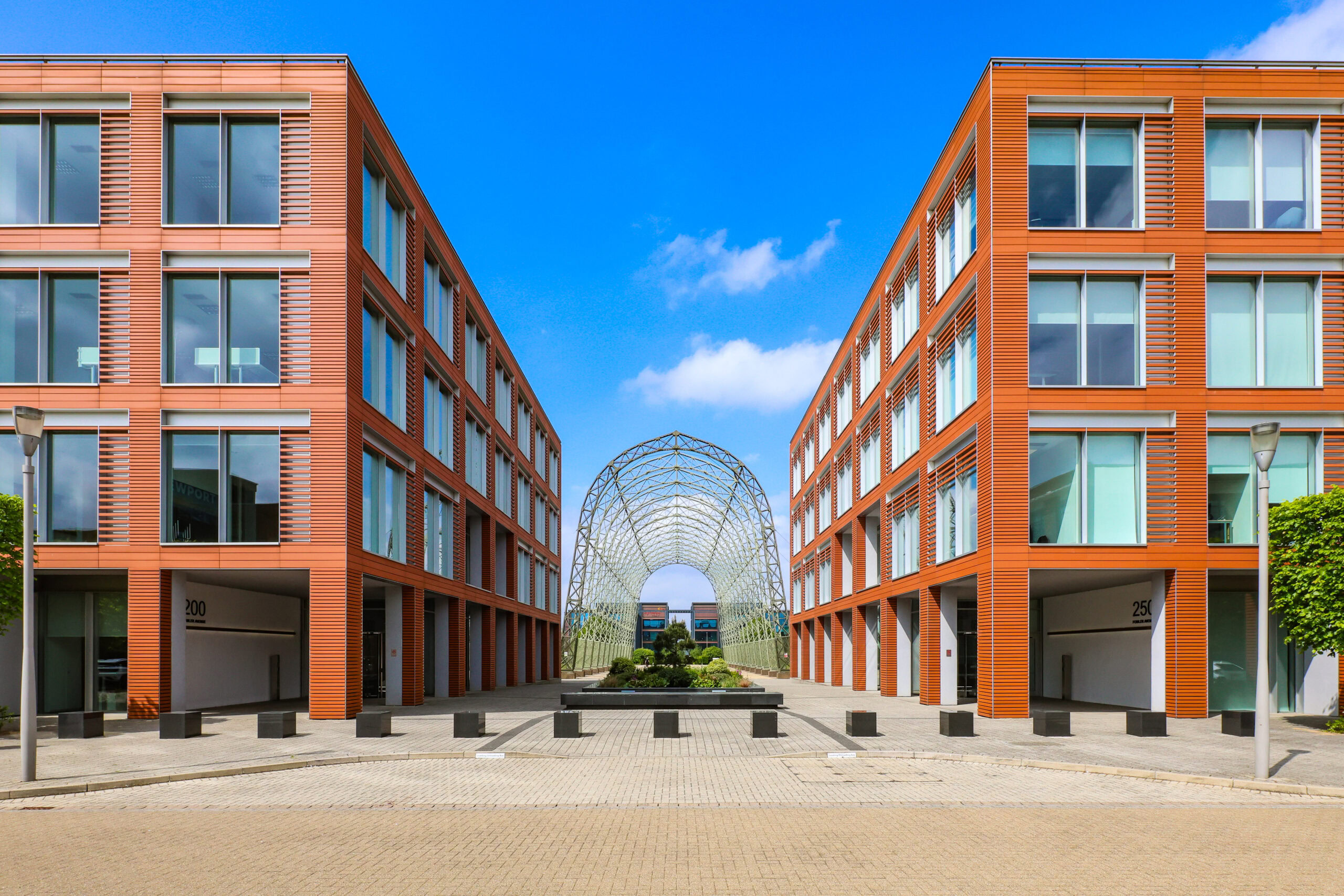 Two modern red-orange office buildings with large windows and a metal arch structure between them.
