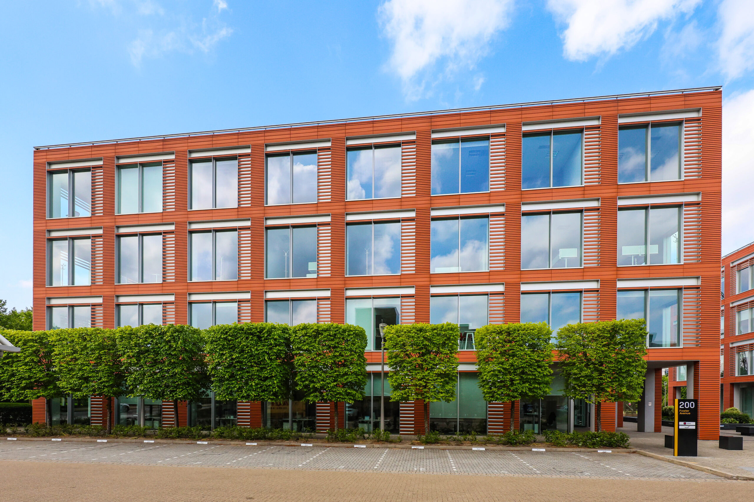 Four-story modern office building with large windows and trimmed trees in front.