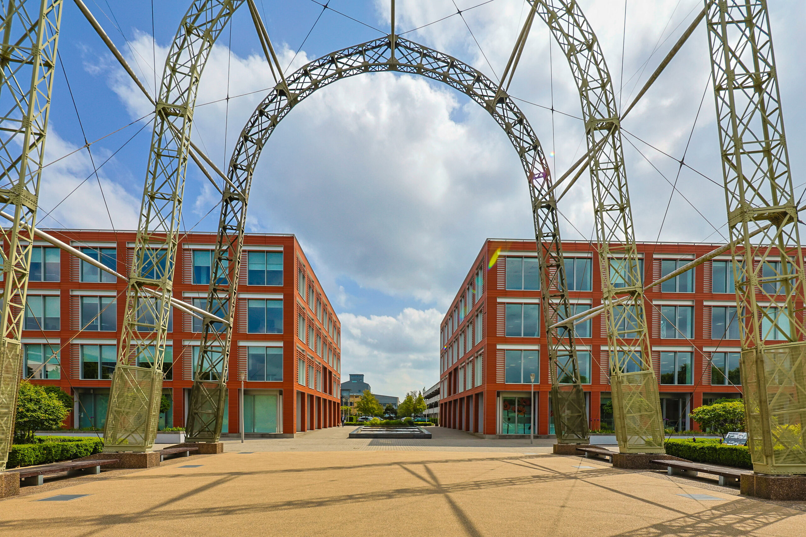 Symmetrical view of two modern brick buildings framed by a large metal arch structure.